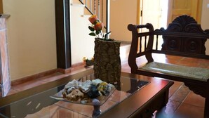 Un banco de madera con intrincados grabados, una mesa de vidrio con un florero y una escalera al fondo.