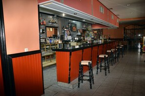 A bar area with stools and a counter, shelves with bottles, and a tiled floor. - Hostal Cesar (Alcaracejos)
