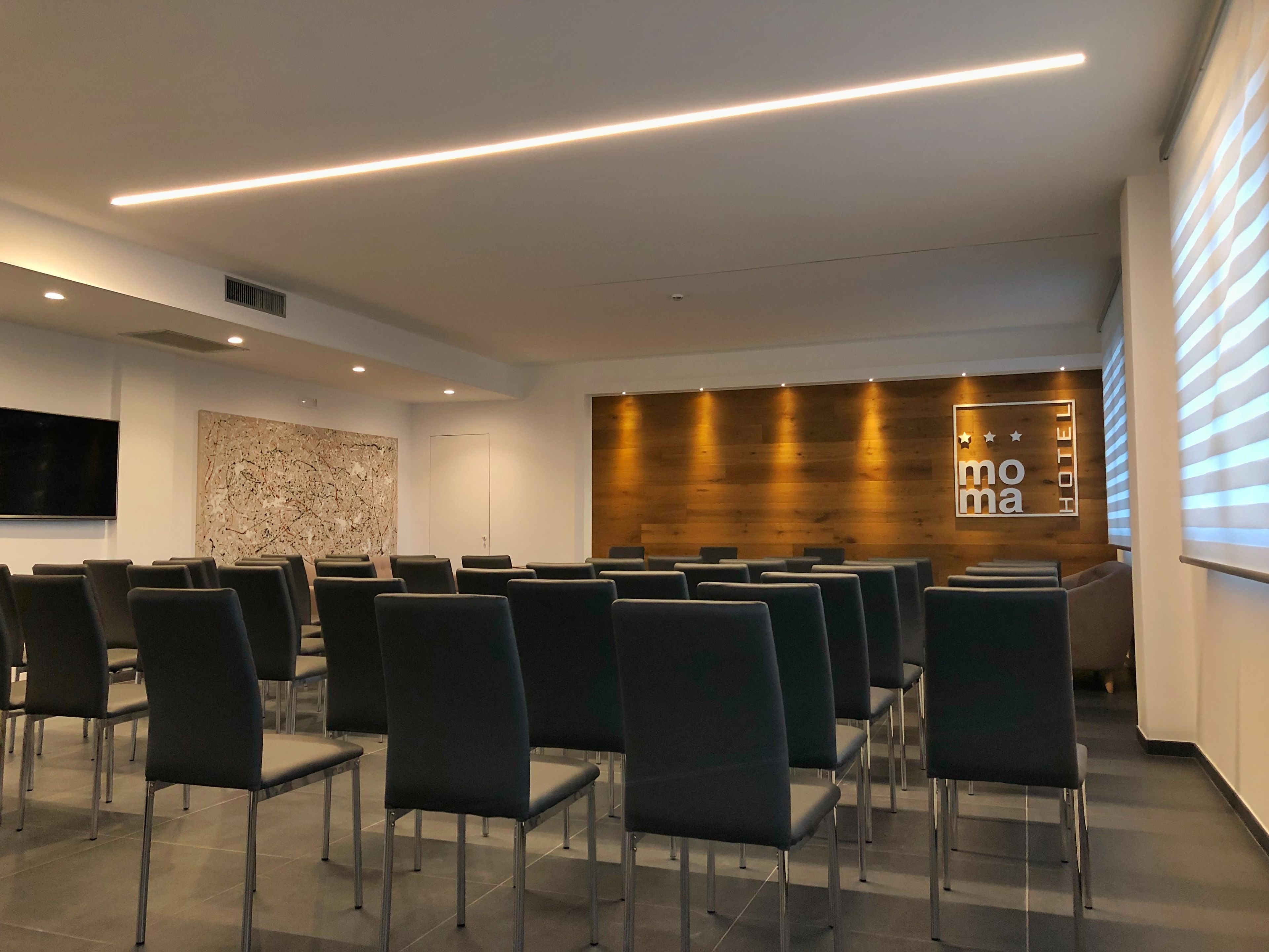Un'accogliente hall di un hotel moderno, con un'area salotto, un grande televisore a schermo piatto, una parete decorativa in legno e un cartello con la scritta "moma HOTEL".