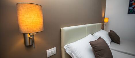 A modern bedroom with a bed, pillows, a wall-mounted lamp, and a painting on the wall.