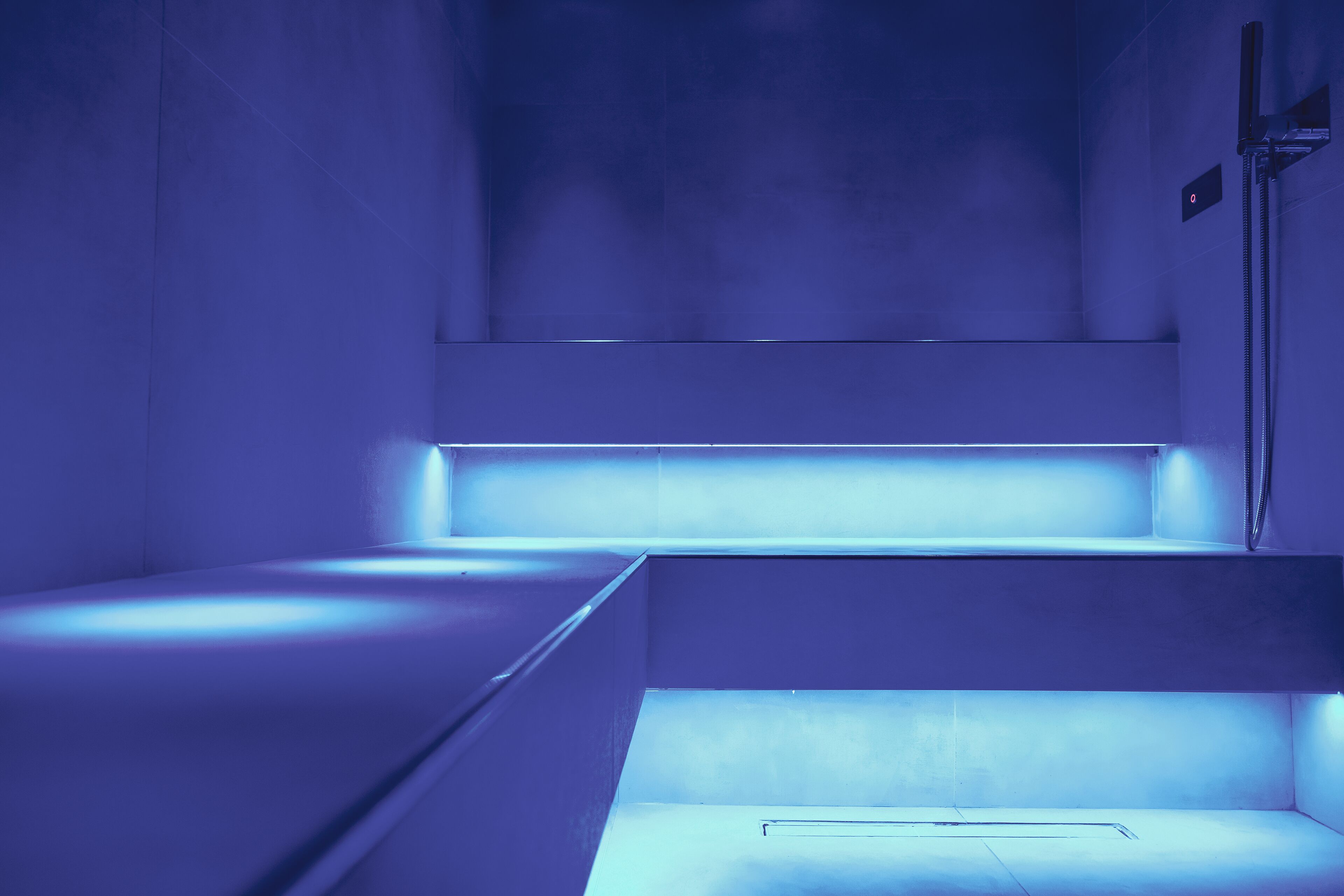 A modern, dimly lit room with a minimalist design, featuring a single bed and a built-in bench.