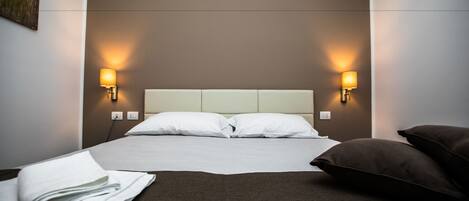 A neatly made bed with white linens, two bedside lamps, and a brown throw blanket.