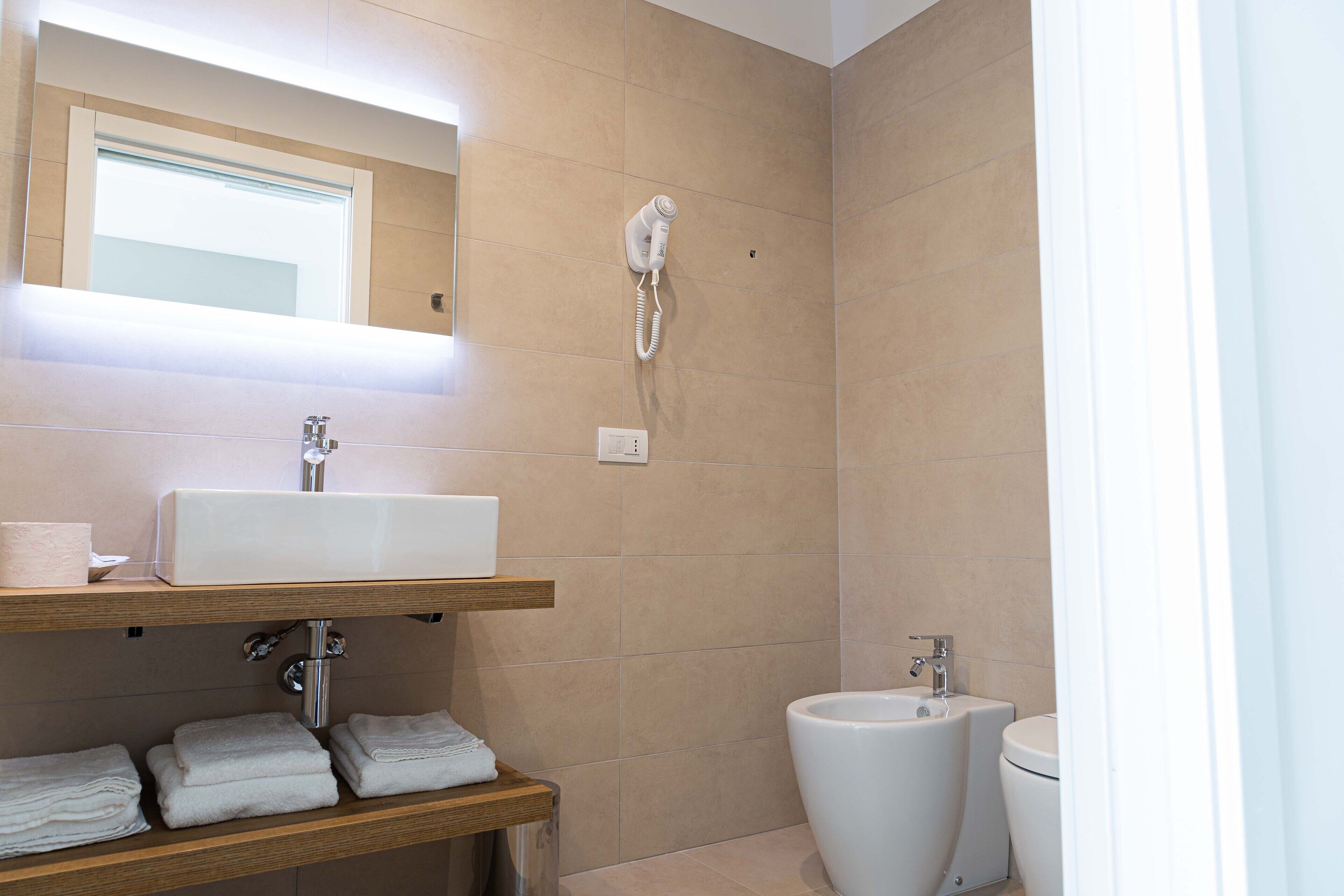 Un bagno con lavandino, specchio, portasci, wc e asciugacapelli montato a parete.