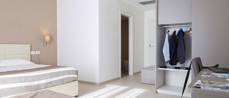 A hotel room with a bed, a desk, a chair, a wardrobe, and a closet.