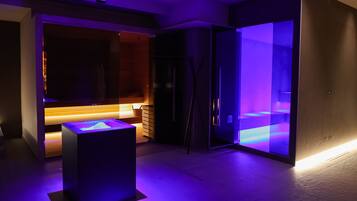 A modern room with a glass partition, a wooden bench, and a black cube with a light.