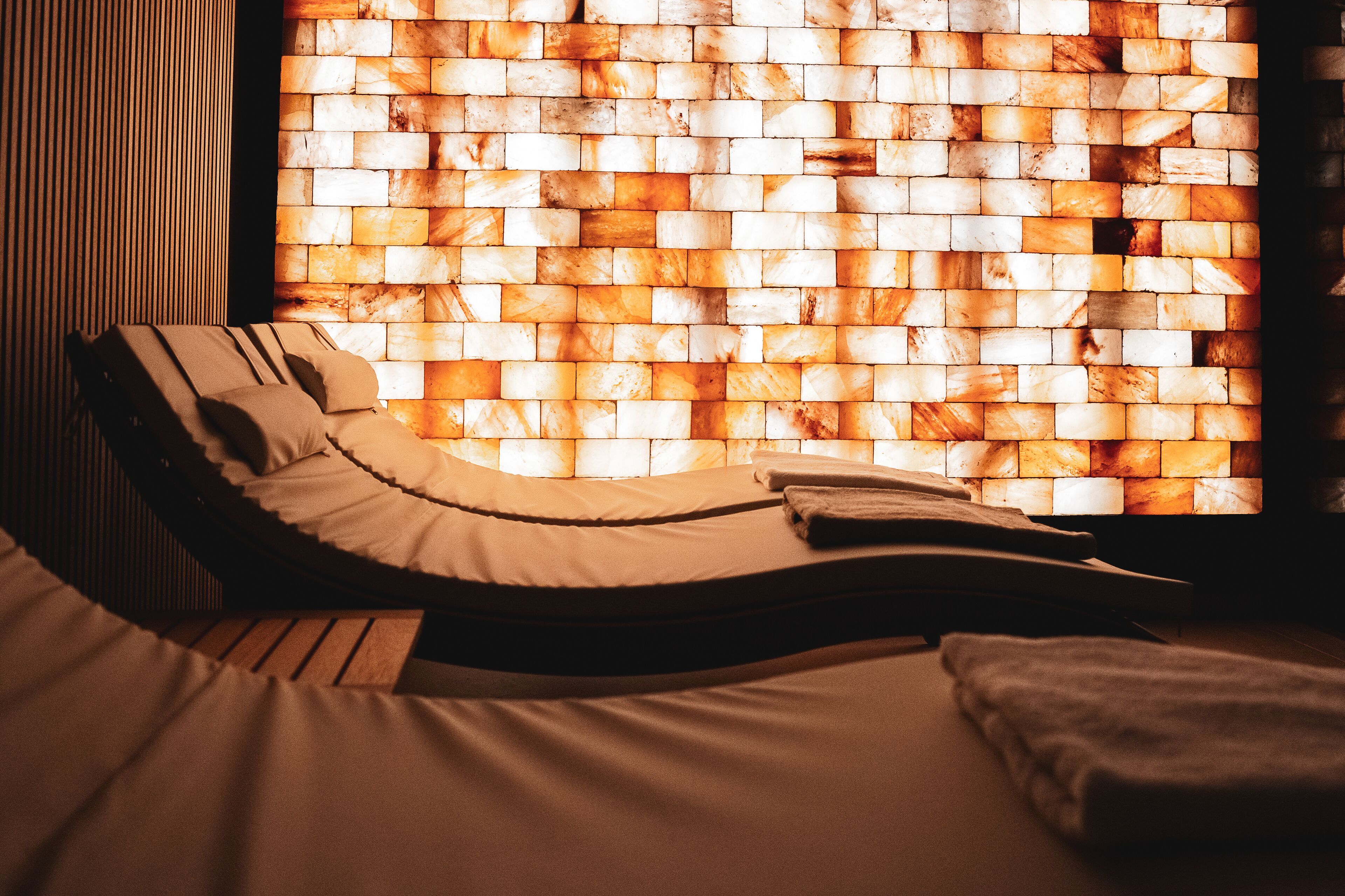 Een kamer met een lange fauteuil, een bed en een muur met een mozaïekpatroon.