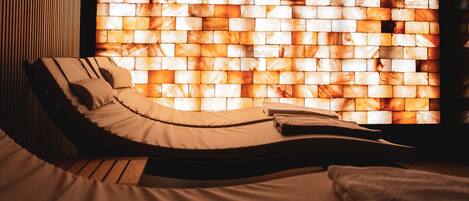 Een kamer met een lange fauteuil, een bed en een muur met een mozaïekpatroon.