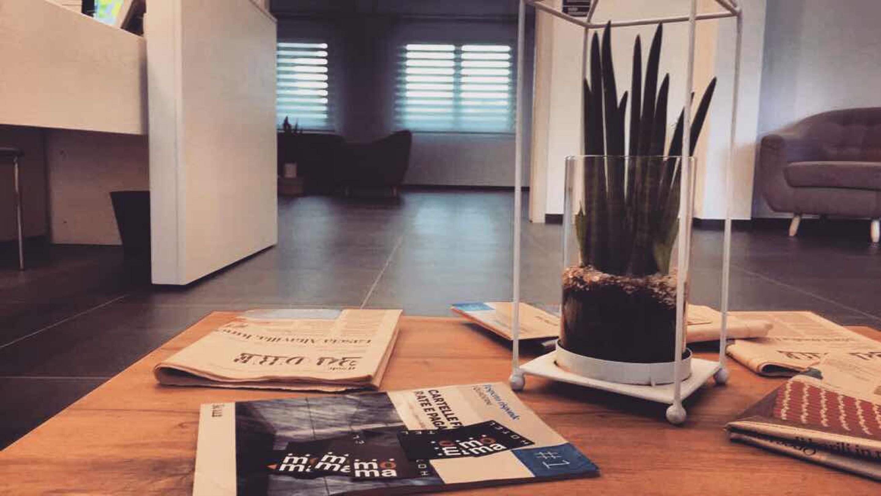 Een modern interieur met een receptiebalie, een plantenstandaard van glas en verspreide tijdschriften op de vloer.