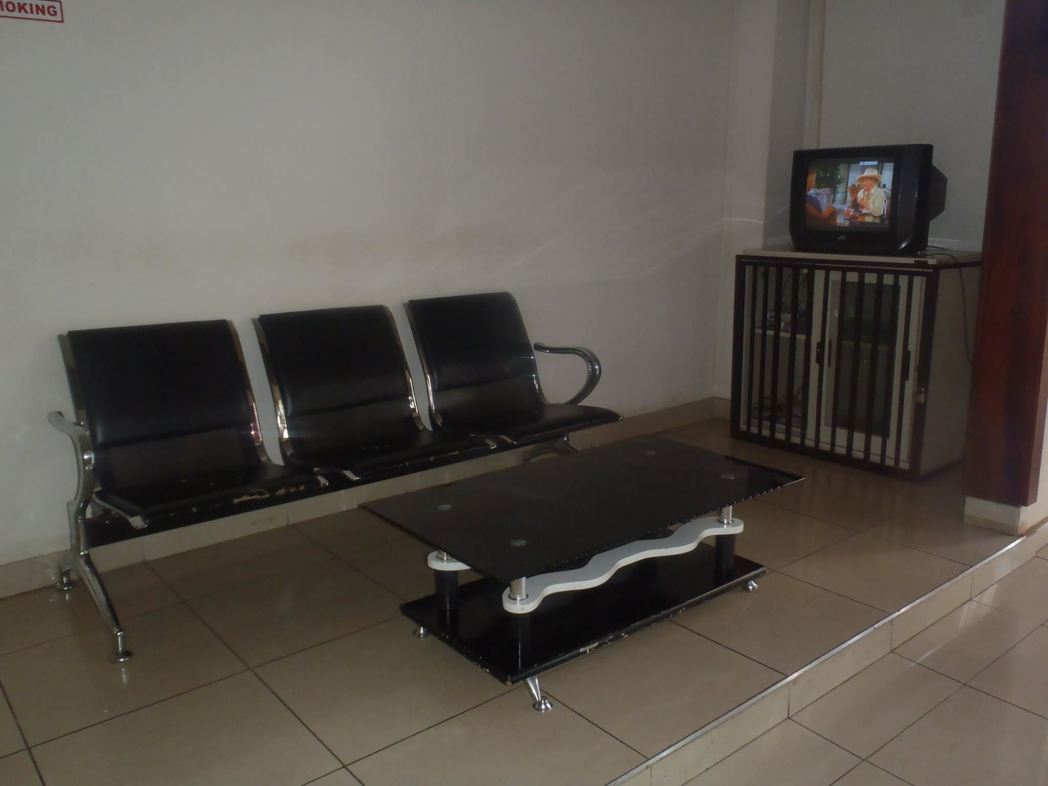 A waiting area with three black chairs and a small table. A television is mounted on a stand to the right.