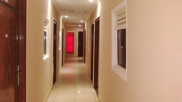 Um corredor com portas em ambos os lados, piso ladrilhado e um fim iluminado em vermelho.