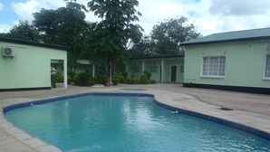 Piscina com borda azulejada, rodeada por um espaço pavimentado e um edifício com fachada verde.