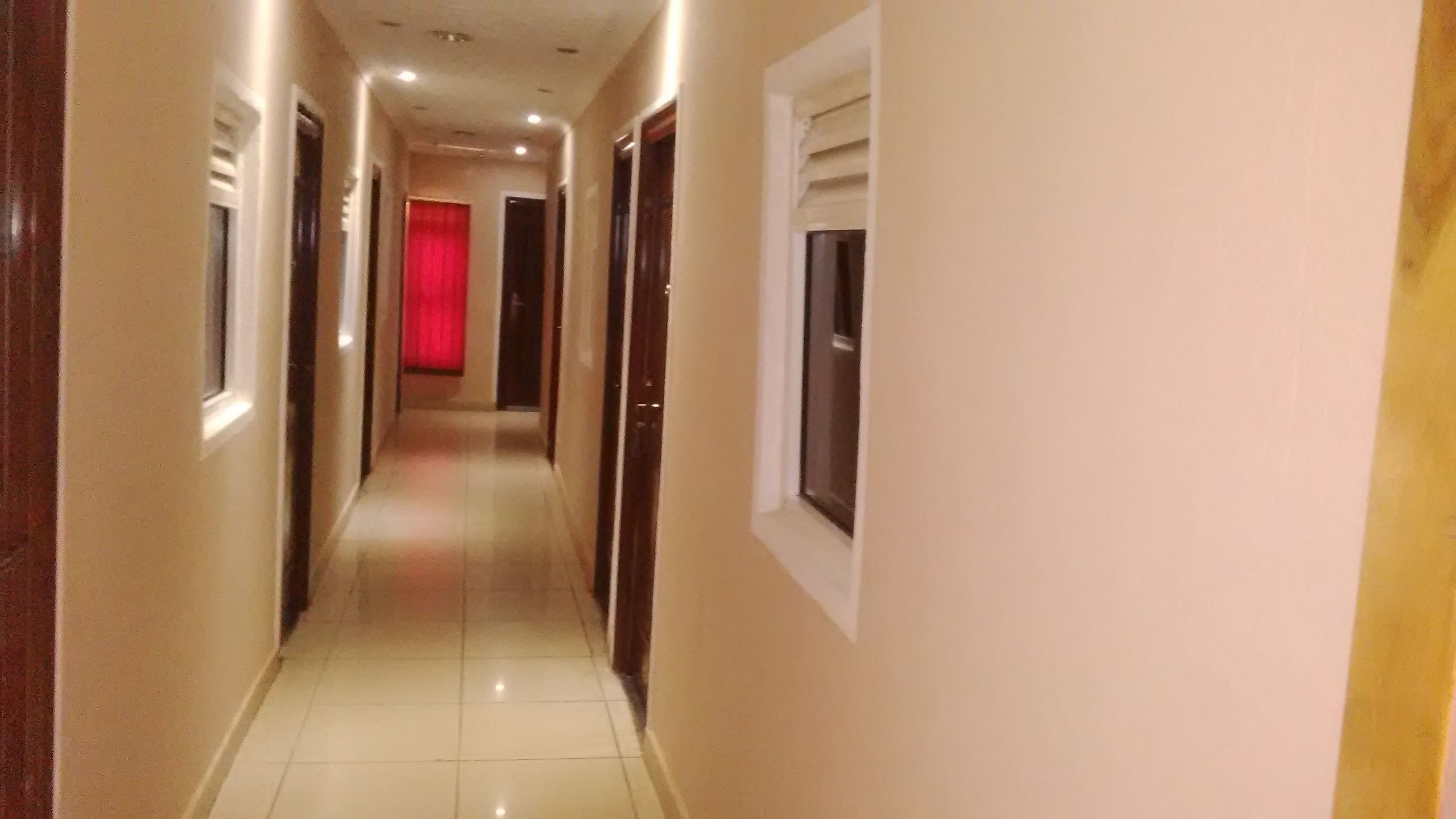 A corridor with doors on both sides, a red curtain at the end, and a window on the right wall.