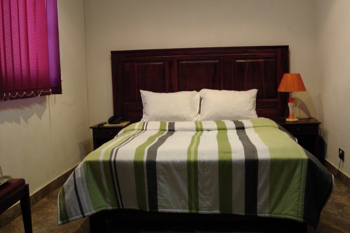 A neatly made bed with a striped bedspread, a wooden headboard, a bedside lamp, and a telephone on the nightstand.