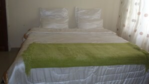 Uma cama de solteiro com um cobertor verde, almofadas brancas e edredom branco.