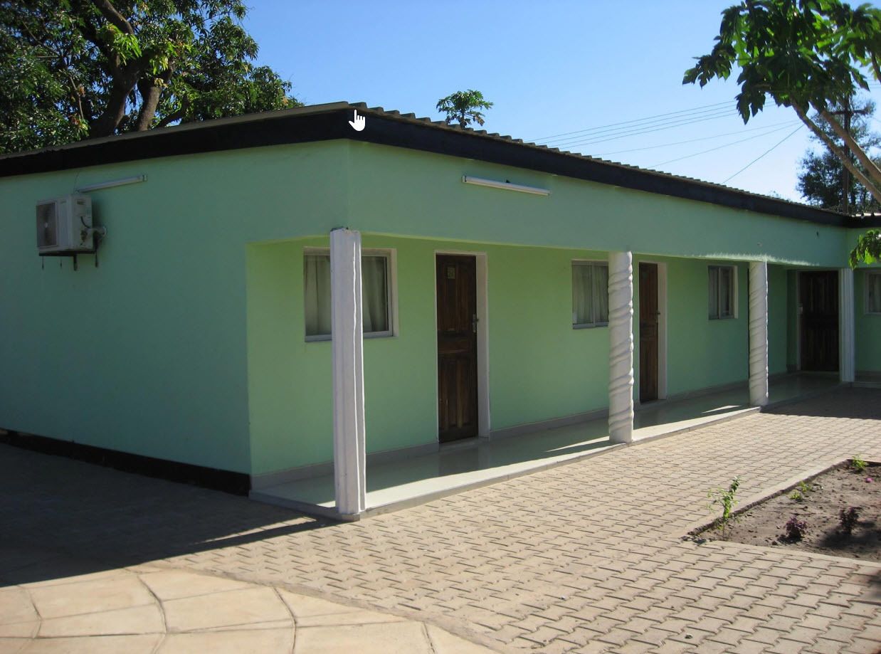 A building with a light green exterior, a tiled entrance, and a paved courtyard.