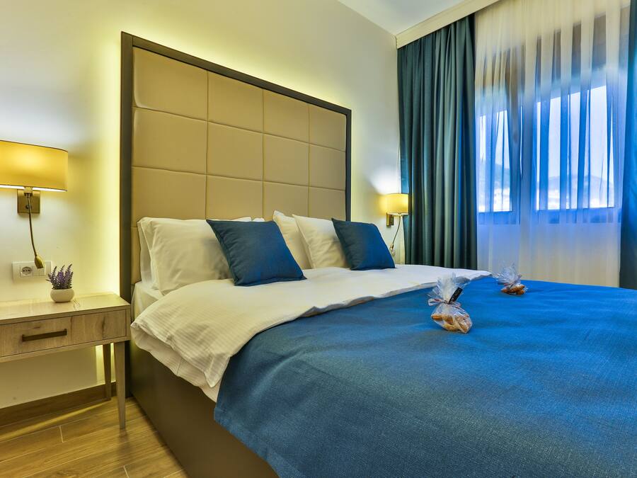 A hotel room with a large bed, a bedside table with a lamp, and a view of the outdoors through the window.