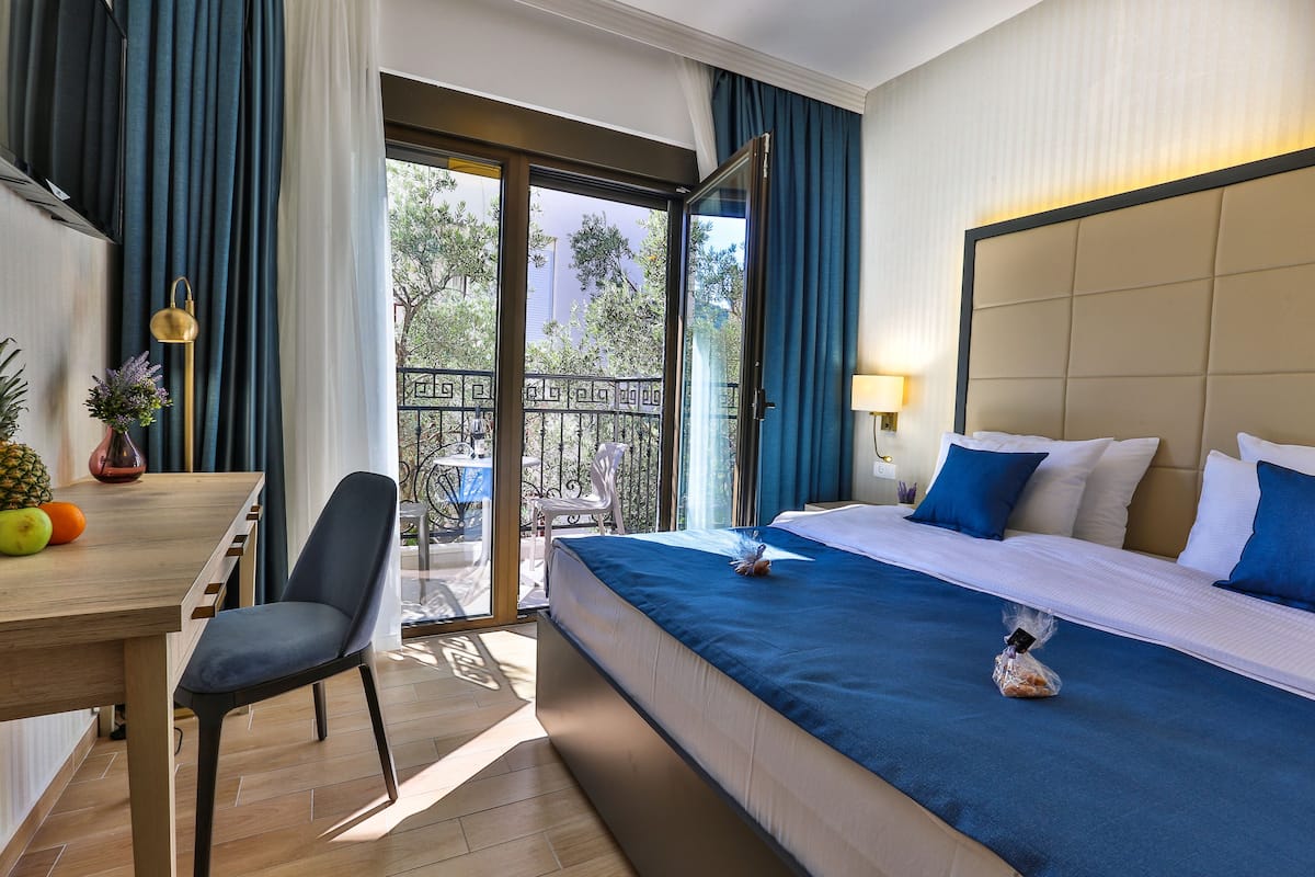 Hotelkamer met een bed, bureau, stoel en balkon met uitzicht op bomen.