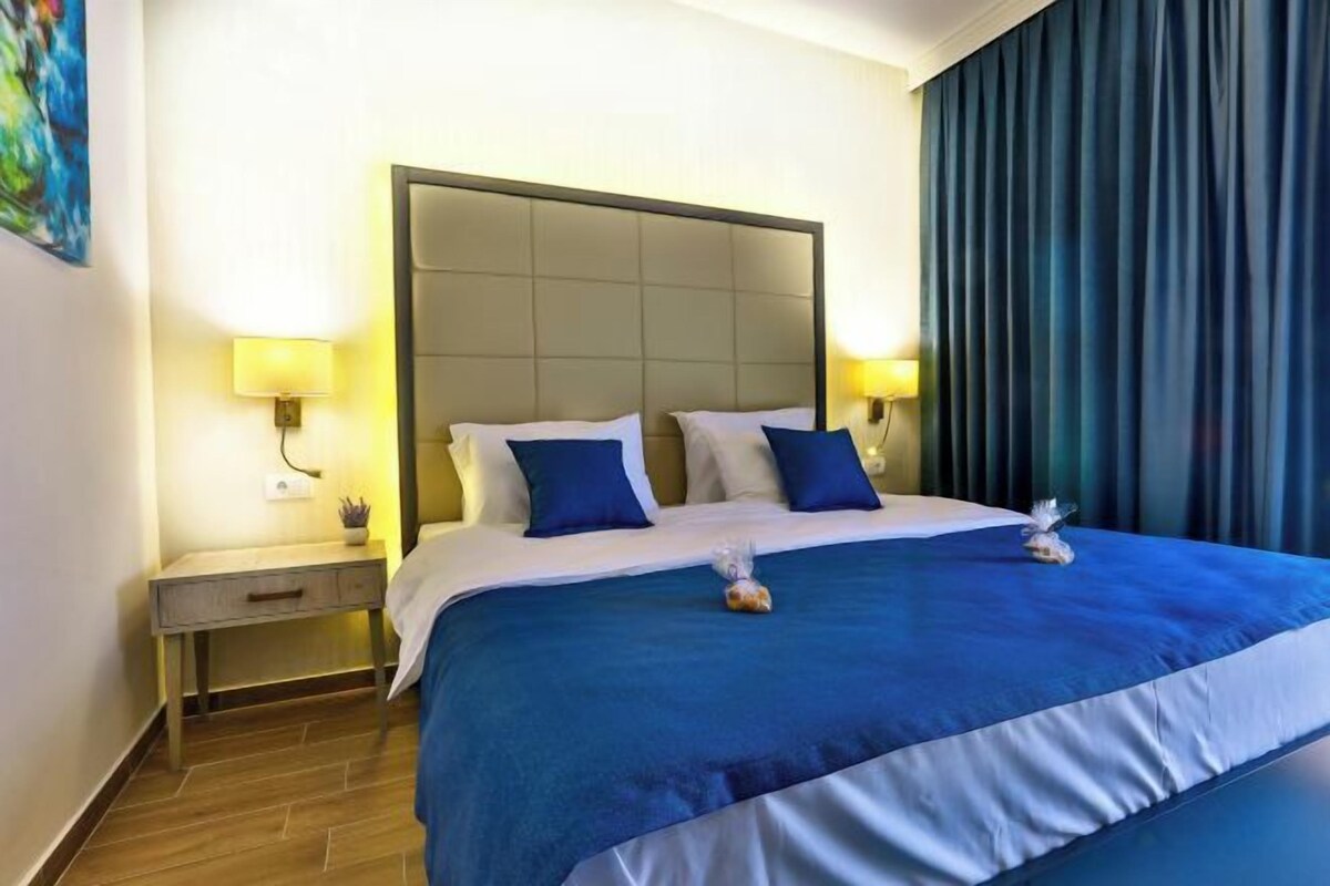 A hotel room with a large bed, two bedside tables with lamps, a headboard, and a curtain.