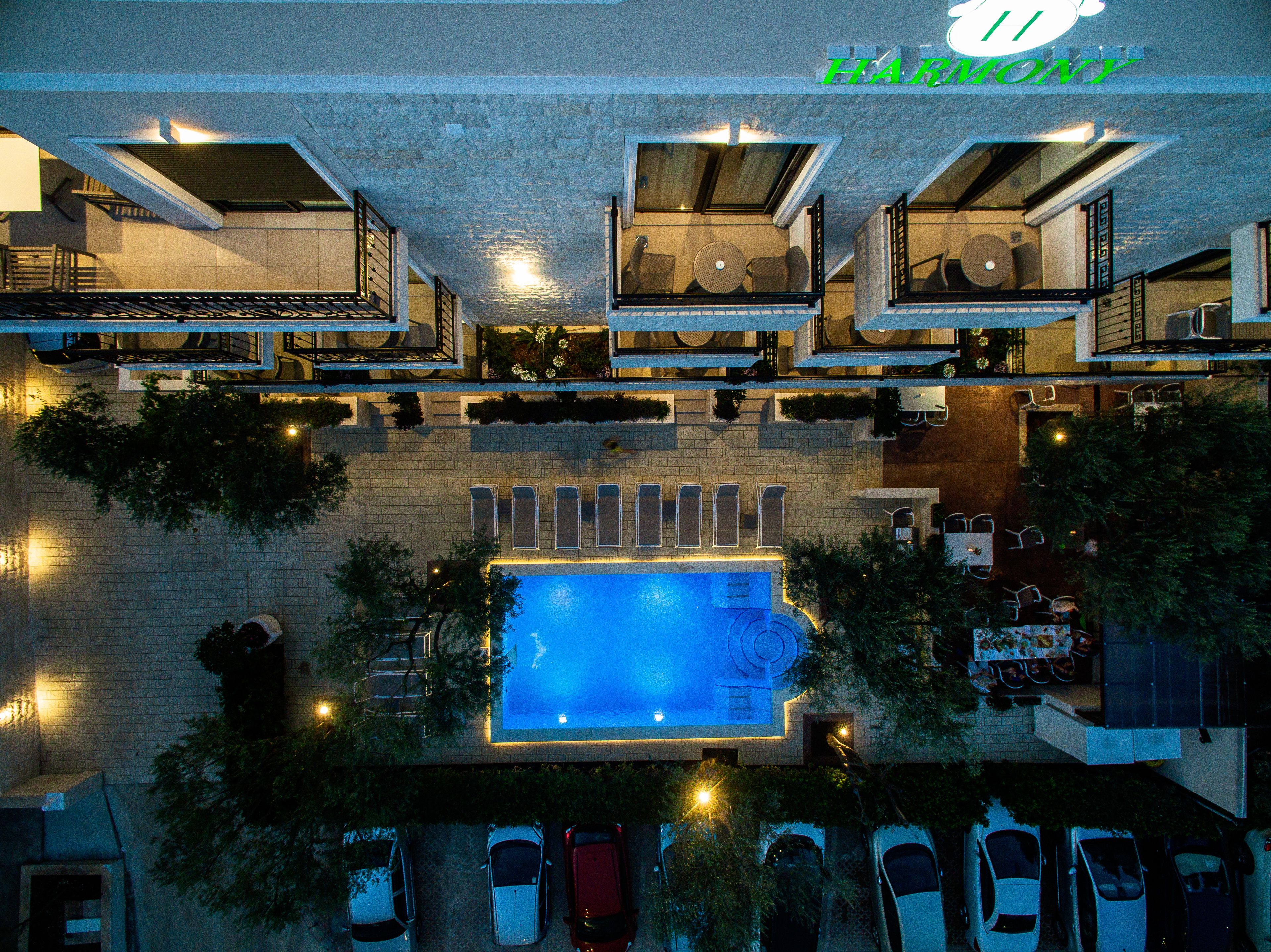 A multi-story hotel with a rooftop pool, outdoor seating, and a sign reading "HARMONY".