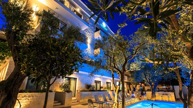 A well-lit outdoor pool area with lounge chairs and a pool table, surrounded by trees and a building with balconies. - Hotel Harmony by Aycon (Petrovac)