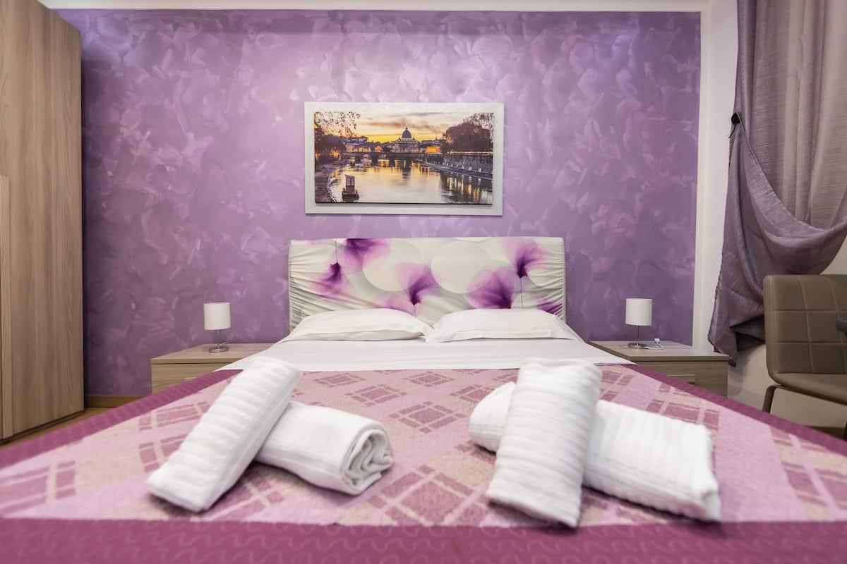 Ein Hotelzimmer mit einem Bett, zwei Nachttischen, einem Sessel und einem Gemälde, das einen Sonnenuntergang über einer Brücke zeigt.