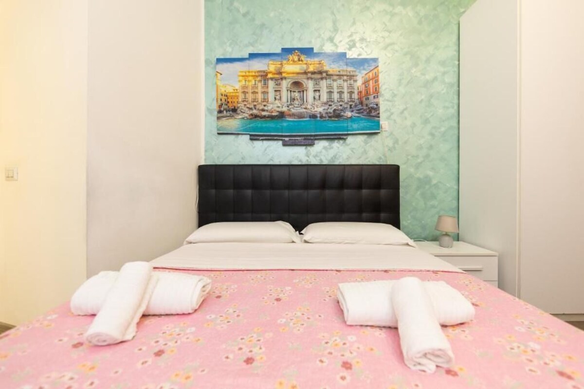 Ein Hotelzimmer mit einem Bett, einem Nachttisch, einer Lampe und einem Gemälde eines bekannten Gebäudes.