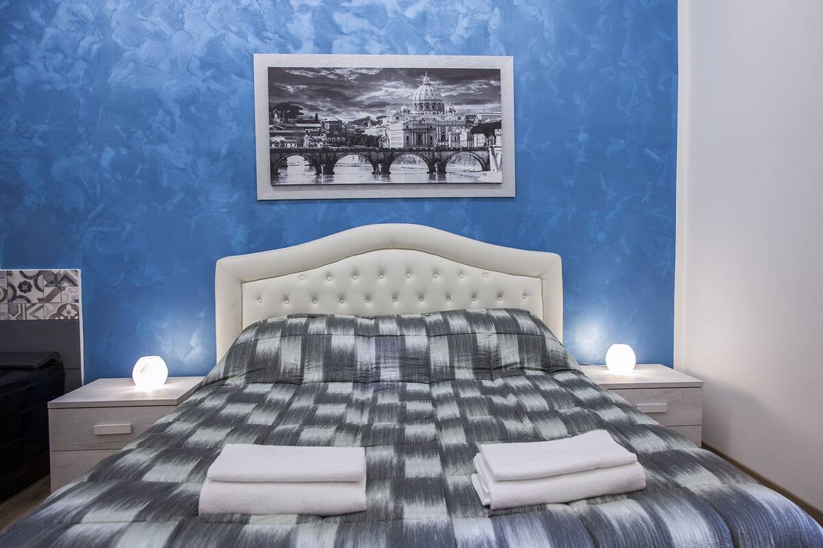 Ein Schlafzimmer mit einem Bett, zwei Nachttischen, einem Wandbild in einem Rahmen und einer blauen, strukturierten Wand.