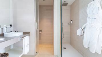 Un baño moderno con cabina de ducha de vidrio, un lavamanos blanco y un perchero con albornoces.