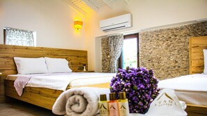 A hotel room with a wooden bed, a small bedside table with toiletries, a window with curtains, and a brick-patterned wall. - Ataol Tatil Ciftligi (Bozcaada)