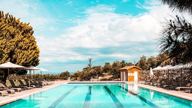 A rectangular swimming pool with clear blue water, surrounded by lounge chairs and umbrellas. - Ataol Tatil Ciftligi (Bozcaada)