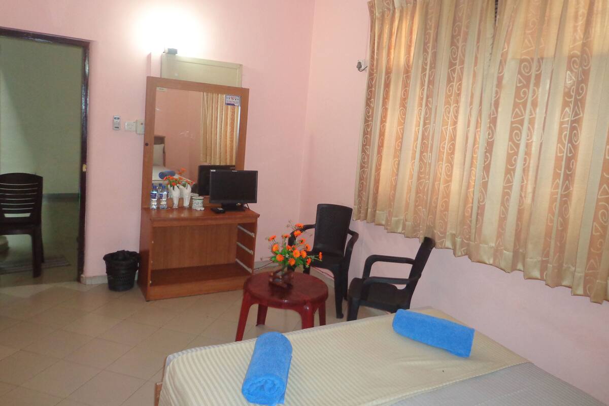 A hotel room with a bed, a desk with a computer, a chair, and a small table with flowers.
