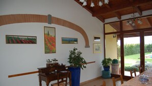 A dining area with a wooden table, chairs, and a potted plant. There are framed pictures on the wall and a view of a garden through a glass door. - Agriturismo Le Rondinelle (Montepulciano)