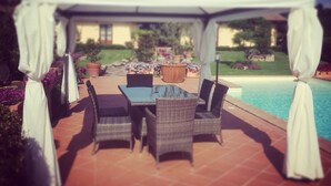 A covered patio area with a table and chairs, a pool, and a house in the background. - Agriturismo Le Rondinelle (Montepulciano)