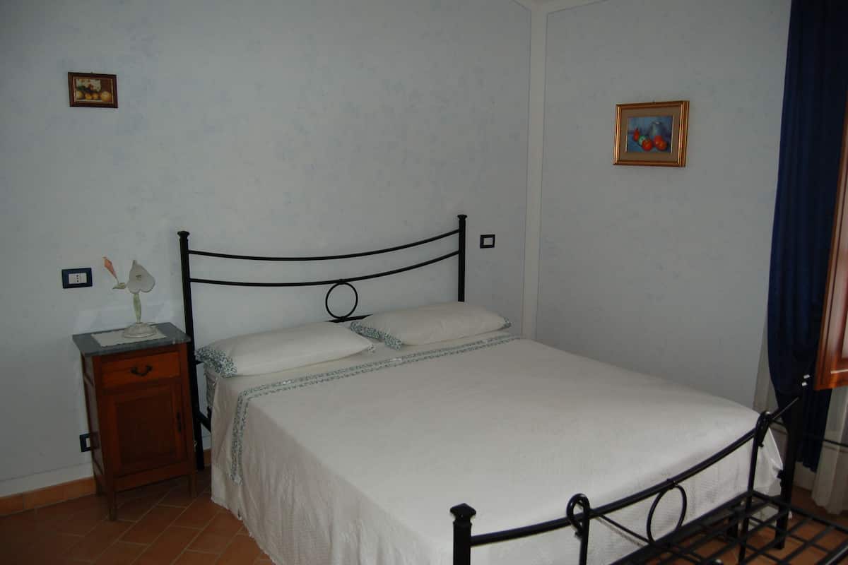 A single bed with a metal frame, a wooden nightstand with a lamp, and two framed pictures on the wall.