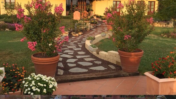 A house with a tiled roof, a stone pathway leading to the entrance, and a pool area with potted plants and flowers. - Agriturismo Le Rondinelle (Montepulciano)