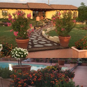 A house with a tiled roof, a stone pathway leading to the entrance, and a pool area with potted plants and flowers. - Agriturismo Le Rondinelle (Montepulciano)