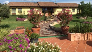 A two-story house with a tiled roof, a paved driveway, and a well-maintained garden with flowering plants. - Agriturismo Le Rondinelle (Montepulciano)