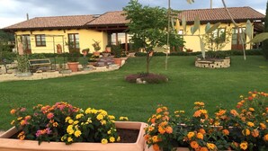 A yellow house with a tiled roof, surrounded by a well-maintained garden with flower beds and a bench. - Agriturismo Le Rondinelle (Montepulciano)
