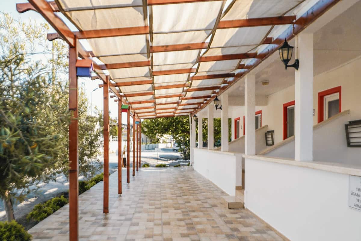 Uma galeria coberta com chão de azulejos estampados e vigas de madeira sustentando um toldo.