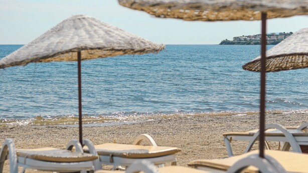 A beach with white lounge chairs and straw umbrellas. - Mali Beach Apart Otel (Seferihisar)