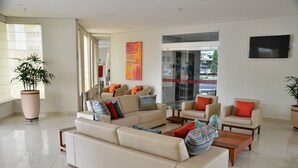 Uma sala de estar moderna com um sofá bege, uma mesinha de centro e uma grande planta em vaso.