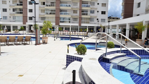 Uma área de piscina no terraço, com várias piscinas, espreguiçadeiras e uma escadaria que dá para um andar superior.