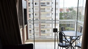 Varanda com mesa e cadeiras, vista de um prédio residencial e um portão de metal.