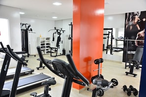 Un gimnasio con máquinas de cardio, equipo de pesas y un espejo grande.