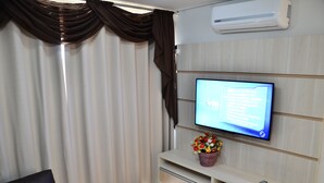 Uma sala de estar moderna com uma televisão de tela plana presa na parede, um rack de madeira abaixo e uma janela com cortinas.