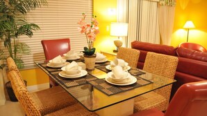A dining area with a glass table set for four, surrounded by wicker chairs and a red sofa. - Coral Cay Resort #2 - 4 Bed 3 Baths Townhome (Kissimmee)