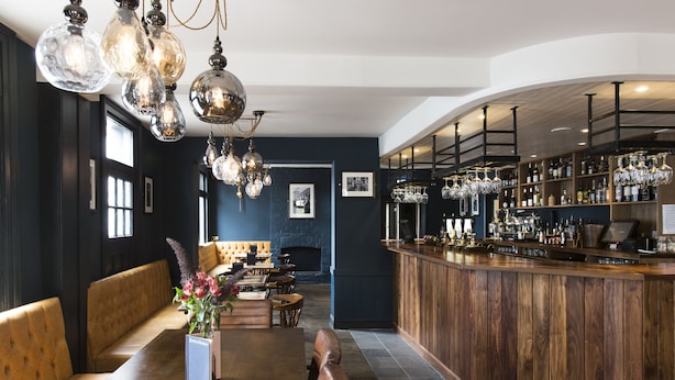 Eine Bar mit Holztresen, hängenden Leuchten und einer Sitzgelegenheit mit einer Bank und einem Tisch.