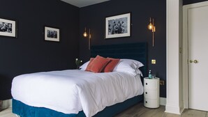 Ein Schlafzimmer mit einem großen Bett, dunklen Wänden, gerahmten Bildern und einem Nachttisch mit einer Flasche.