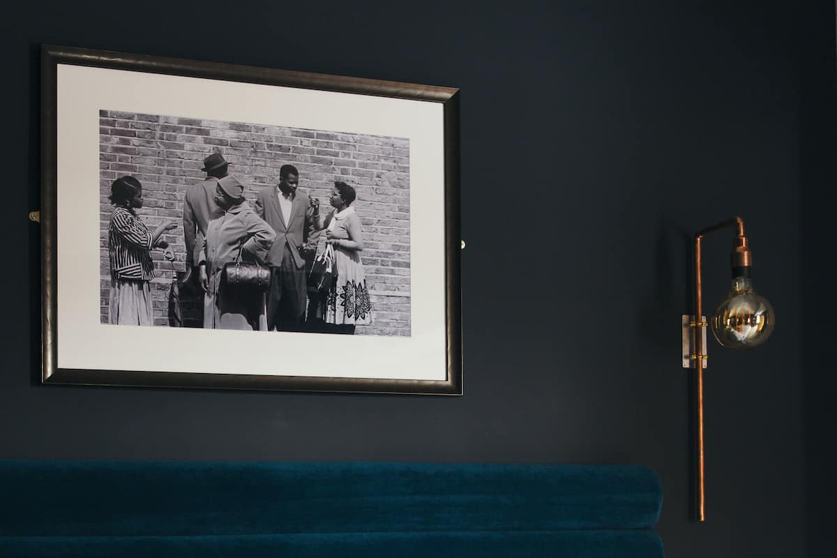 Een slaapkamer met een donkerblauwe hoofdbord, een zwart-wit foto in een lijst aan de muur, en een enkel rode kussen op het bed.