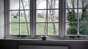 A room with a large window overlooking a grassy field and trees. - Hurtwood Hotel (Guildford)